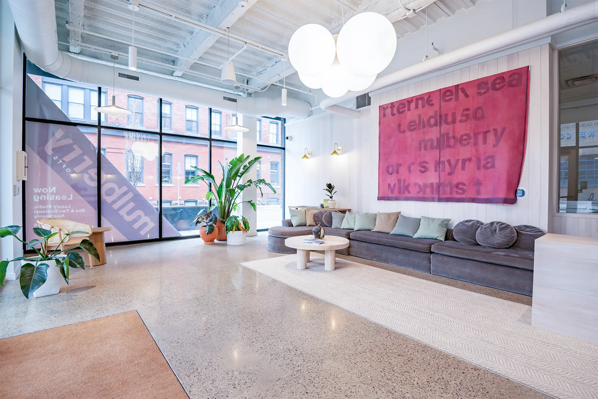 Interior view of a sunlit common area with lounge seating and large windows.